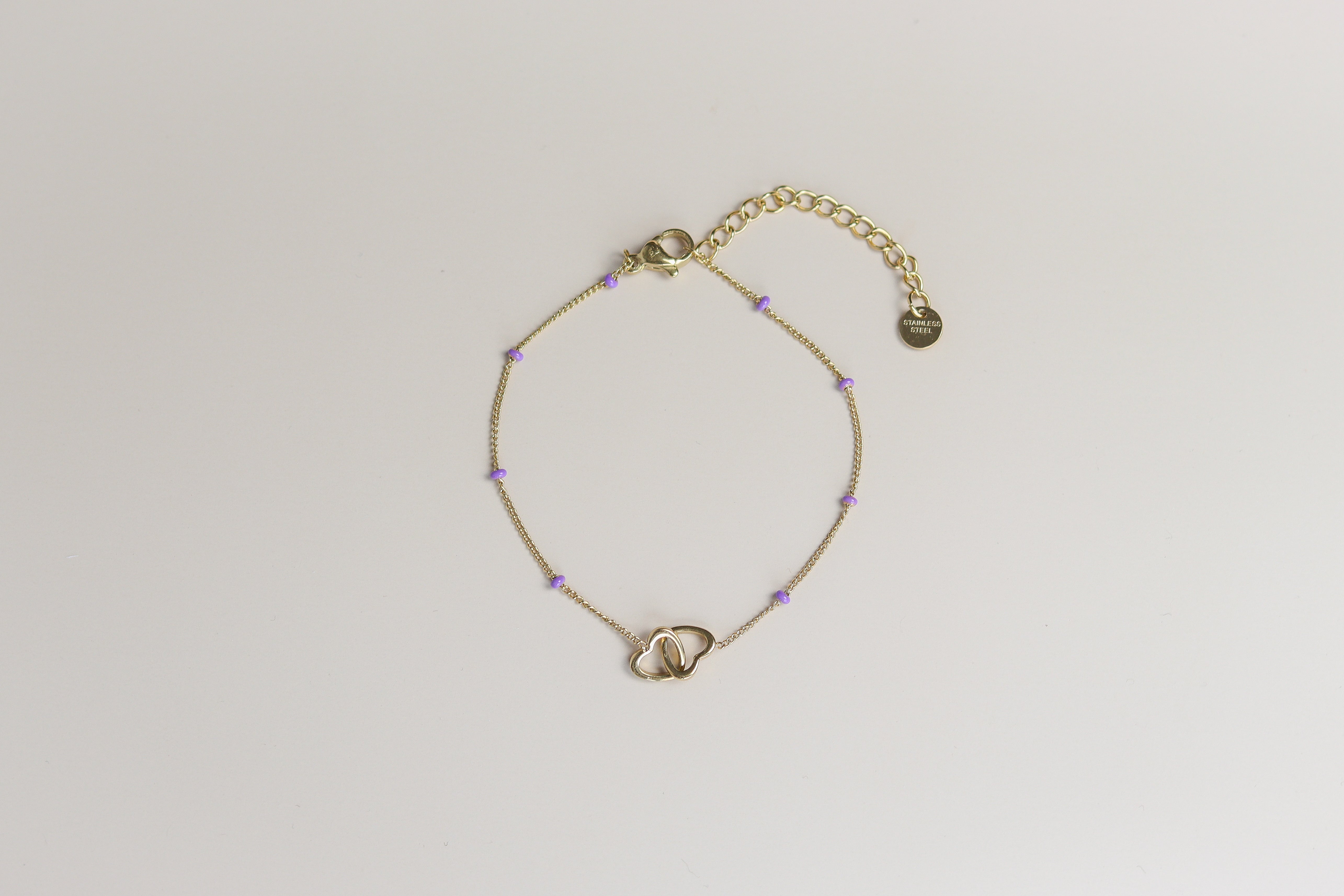 Gouden armband met verbonden hartjes en paarse kraaltjes