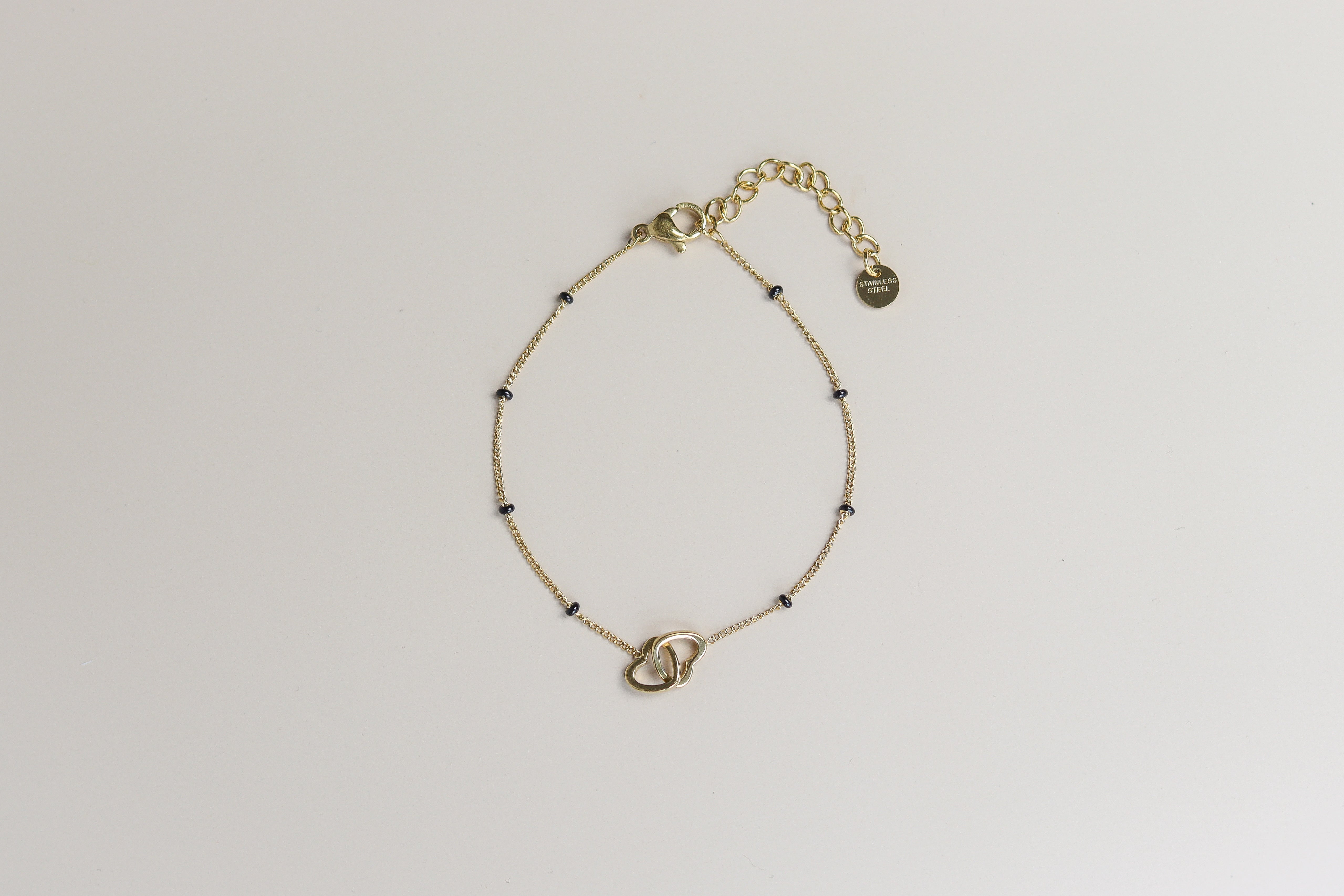 Gouden armband met verbonden hartjes en zwarte kraaltjes